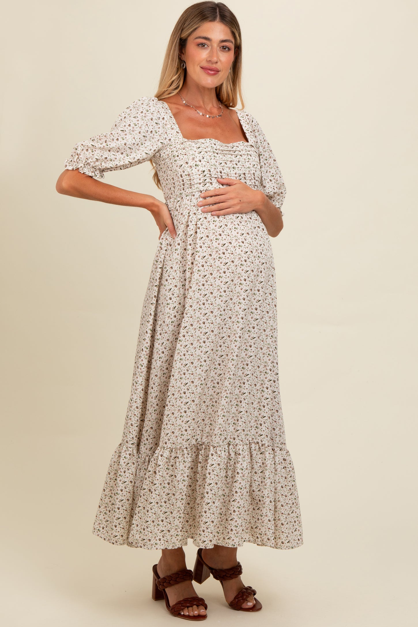 woman wearing a cream floral print maternity dress with puff sleeves and a tiered hem, showing her baby bump