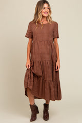 woman wearing a brown gingham maternity dress with tiered ruffles and short sleeves, standing with one hand on her hip