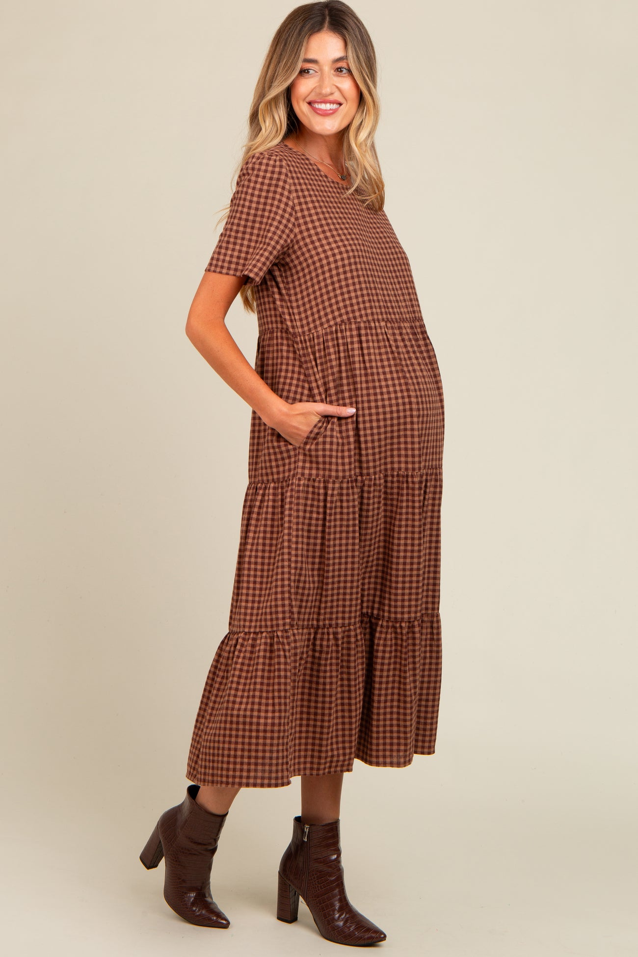 woman wearing a brown checkered maternity dress with short sleeves and tiered skirt, showing a baby bump