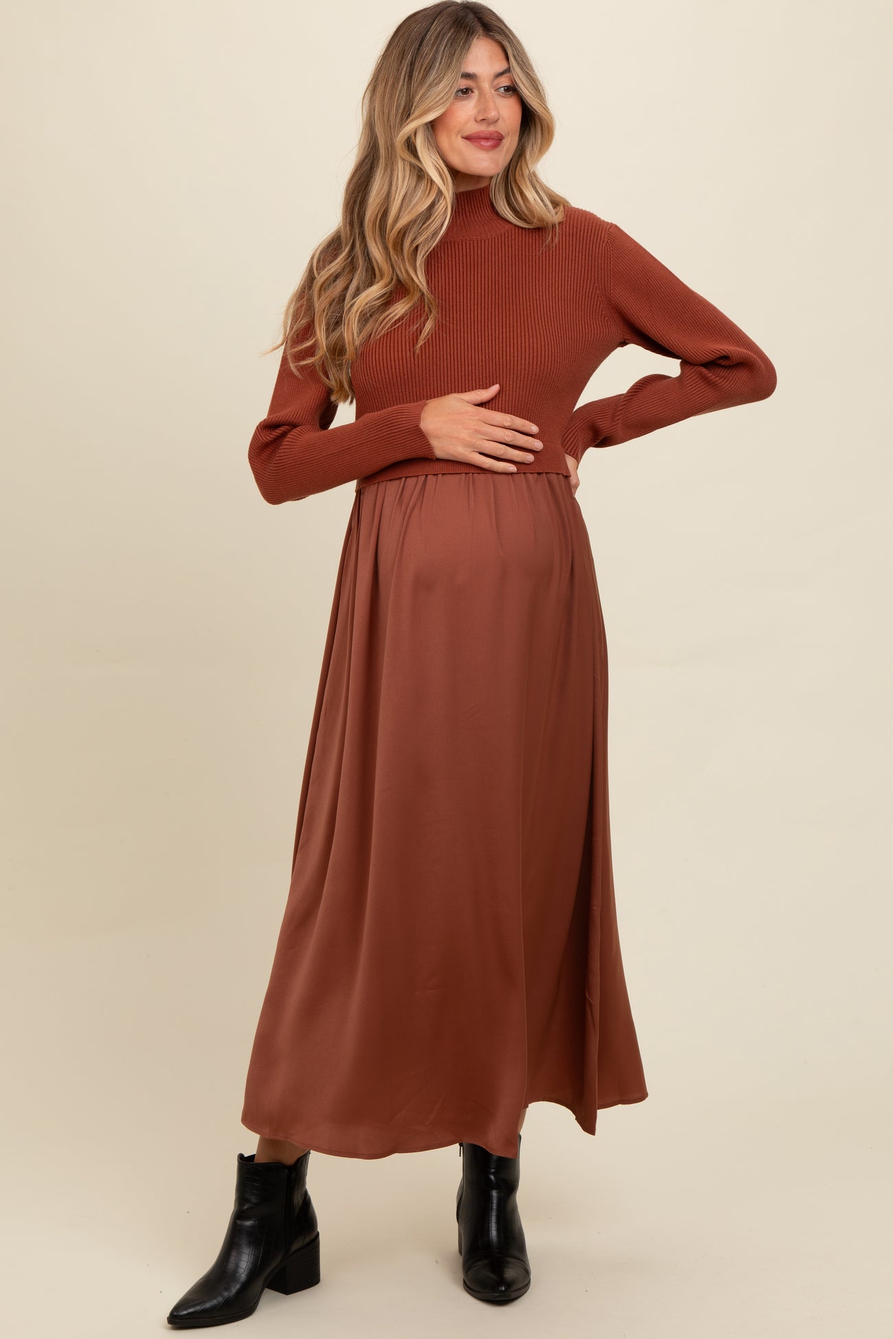 woman wearing a rust-colored ribbed turtleneck maternity dress with a flowing skirt and holding her baby bump