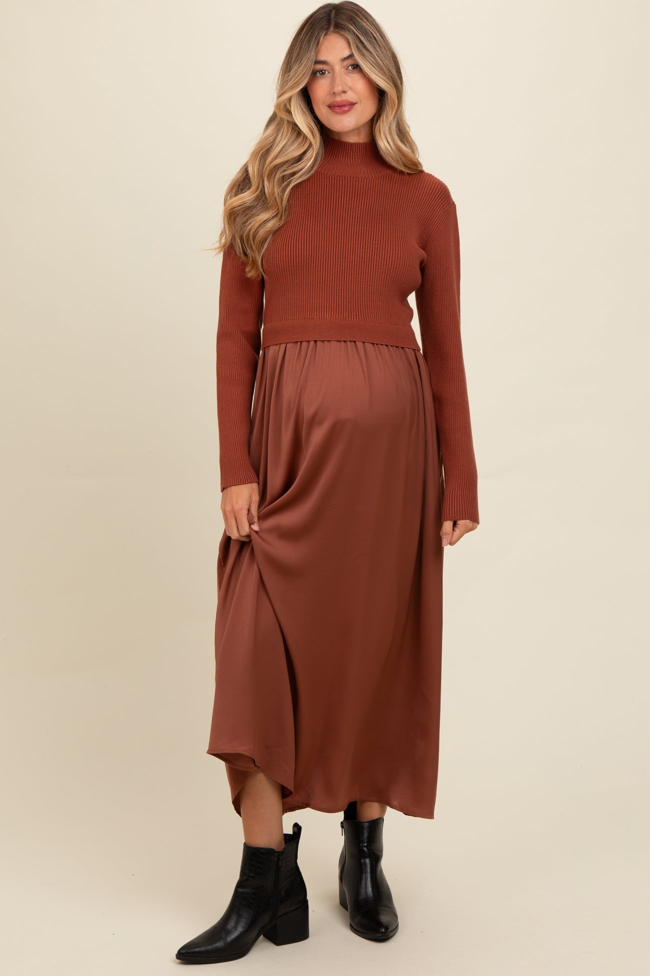 woman wearing a brown ribbed turtleneck maternity top and a flowy brown satin maternity skirt, with a visible baby bump
