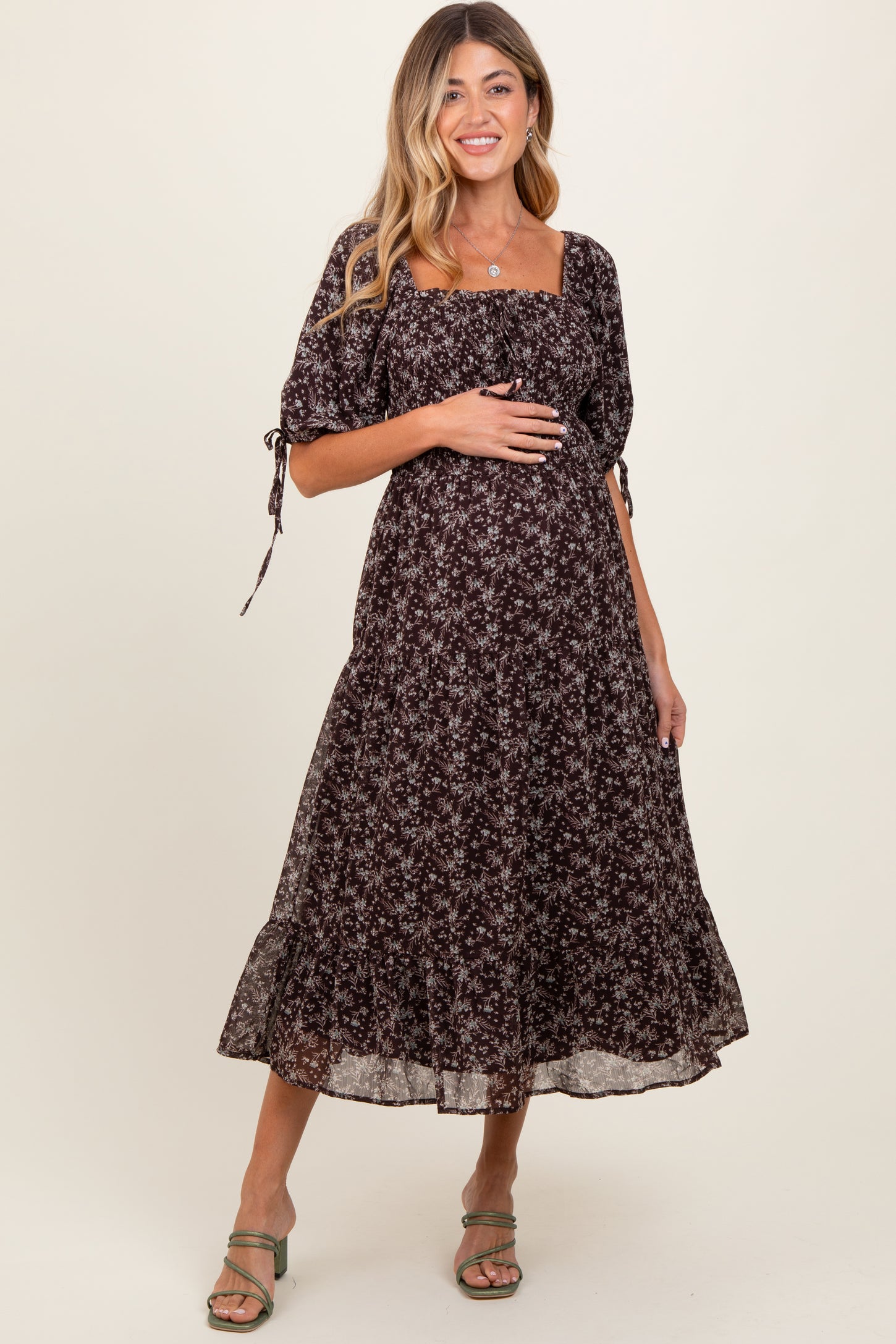 woman wearing a dark floral maternity dress with a square neckline and puff sleeves, holding her baby bump
