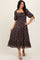 woman wearing a dark floral midi dress with puff sleeves and tie details on the sleeves, standing on a neutral background
