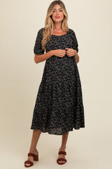 woman wearing a black floral maternity dress with short puff sleeves and a flowy skirt, standing and smiling