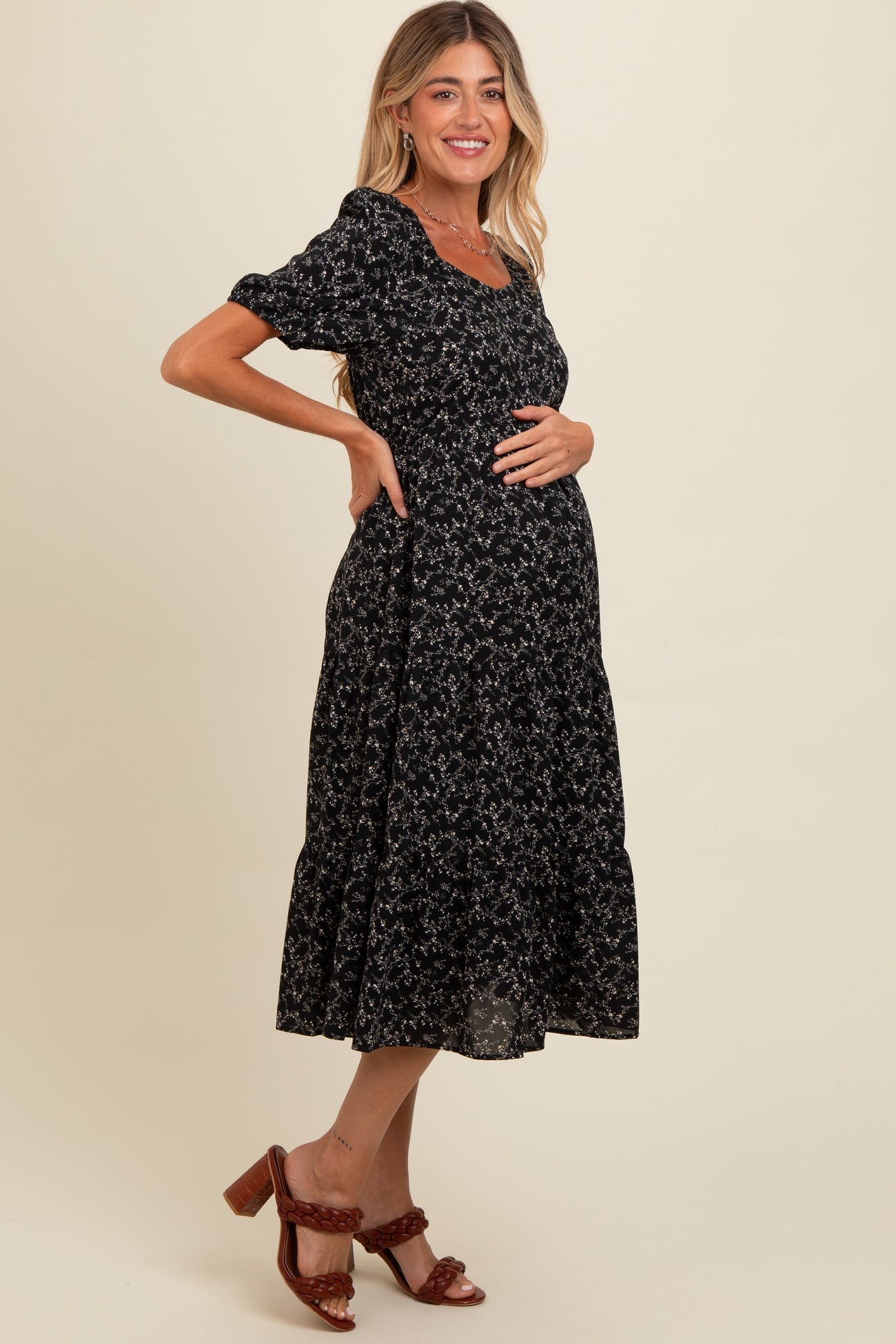 woman wearing a black floral maternity dress with short sleeves and a tiered skirt, showing her baby bump