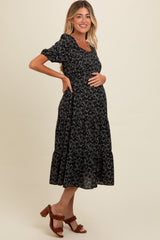 woman wearing a black floral maternity dress with short sleeves and a tiered skirt, showing her baby bump