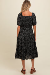woman wearing a black floral print maternity dress with short puff sleeves and a tiered skirt, showing the back view
