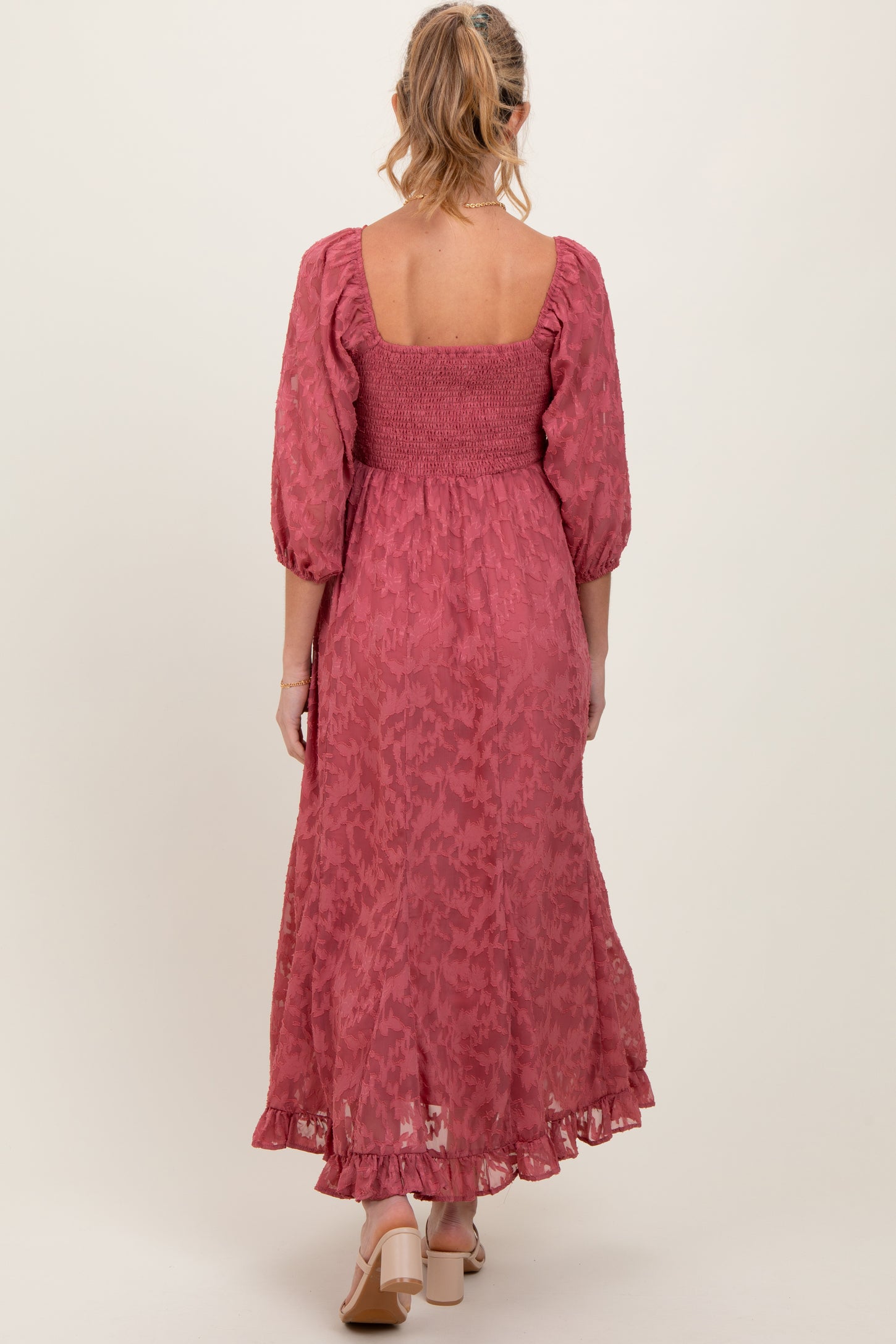 woman wearing a long pink maternity dress with puff sleeves and a smocked bodice, viewed from the back