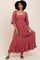 woman wearing a pink smocked maxi dress with puff sleeves and ruffled hem, standing and smiling