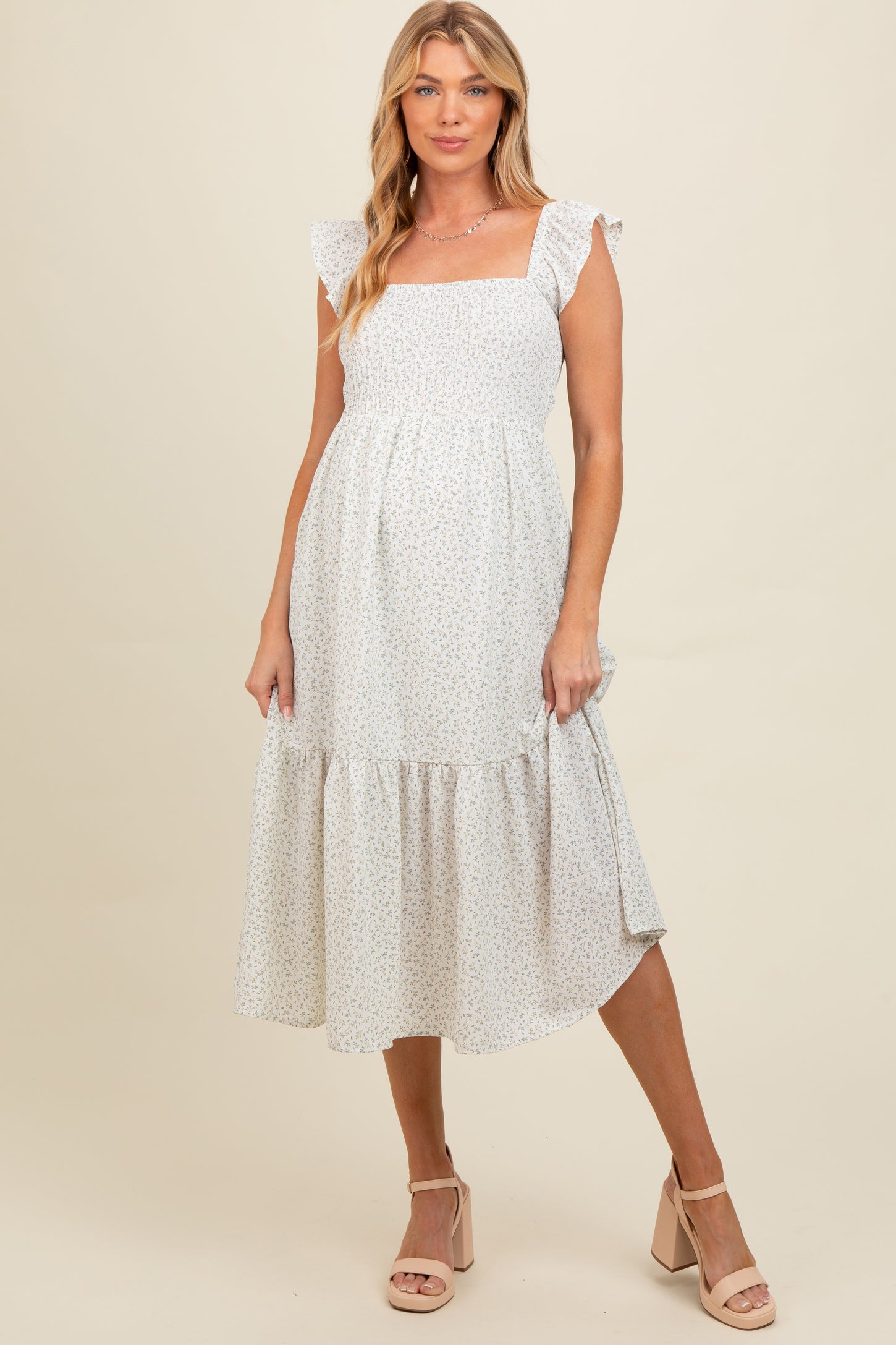 woman wearing a white floral print maternity dress with ruffle straps and tiered hem, showcasing her baby bump