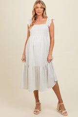 woman wearing a white floral print maternity dress with ruffle straps and tiered hem, showcasing her baby bump