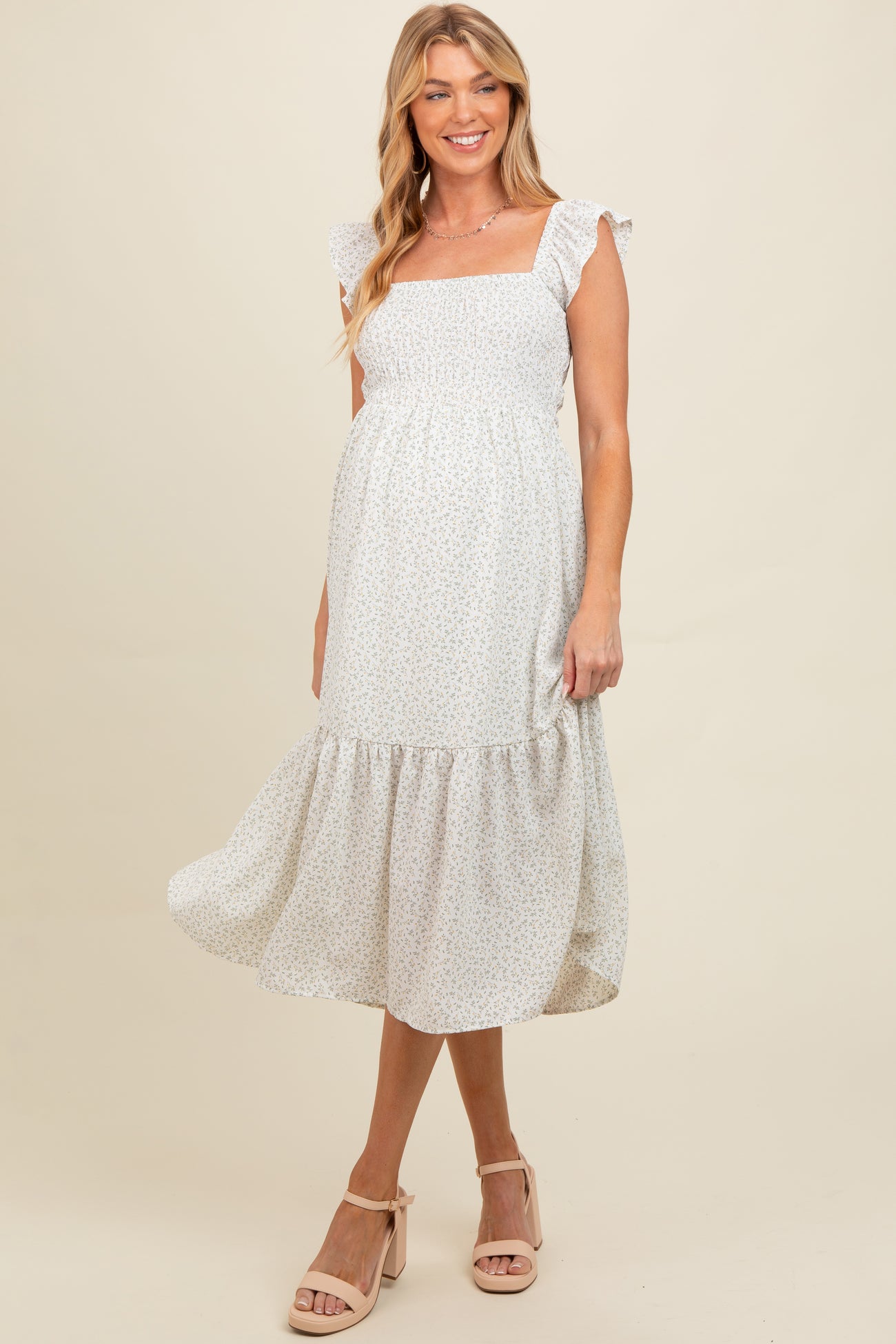woman wearing a white floral maternity dress with ruffled sleeves and a tiered skirt, showing her baby bump