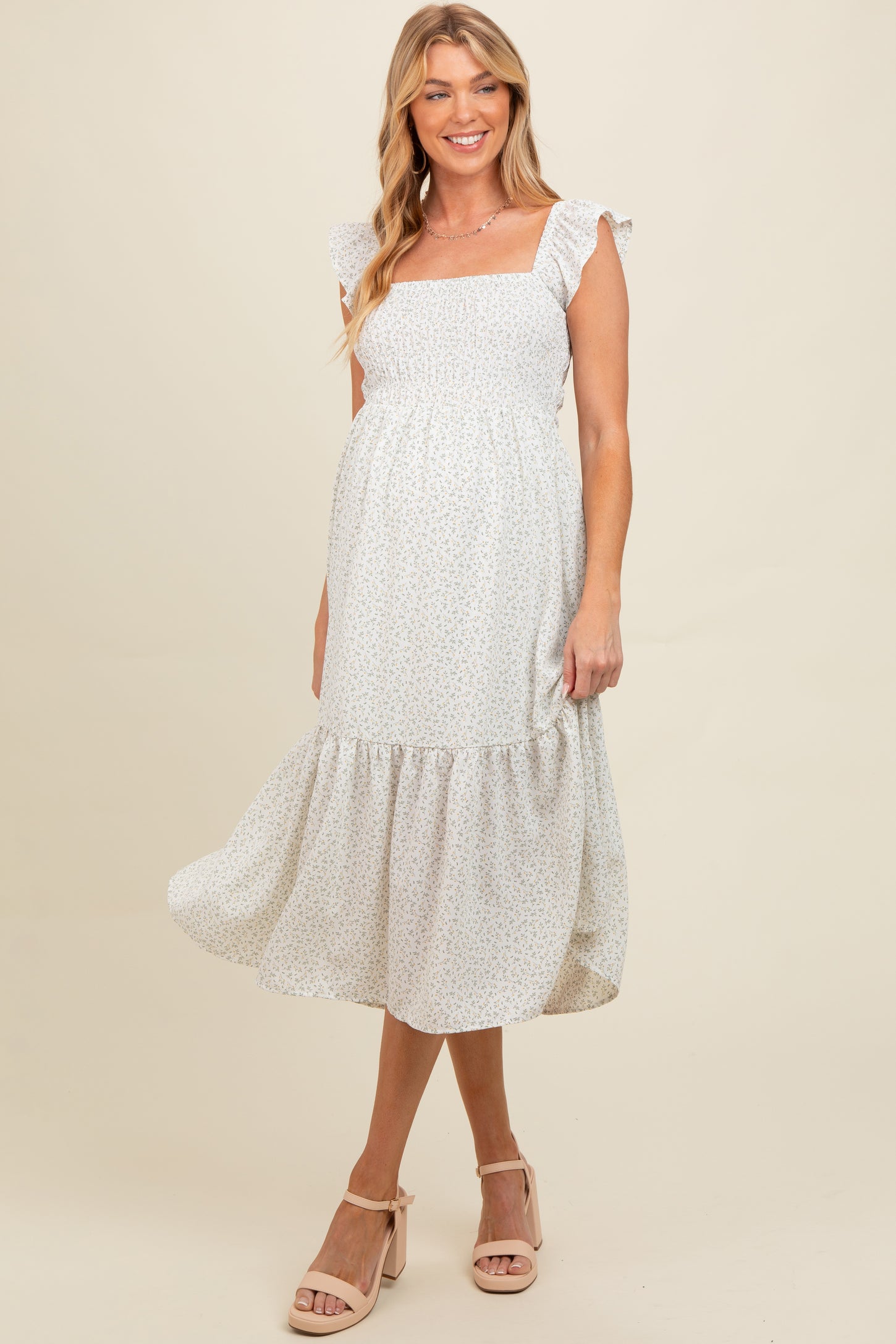 woman wearing a white floral maternity dress with ruffled sleeves and a tiered skirt, showing her baby bump