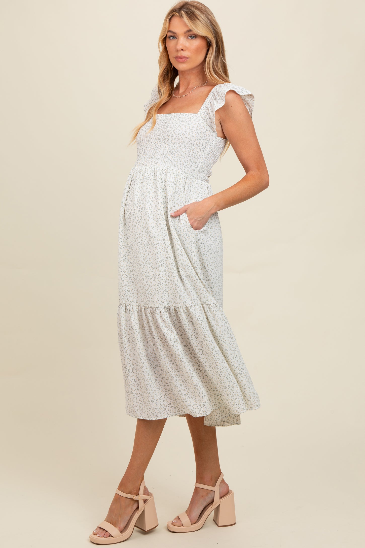 woman wearing a white floral maternity dress with ruffled sleeves and pockets, showcasing her baby bump