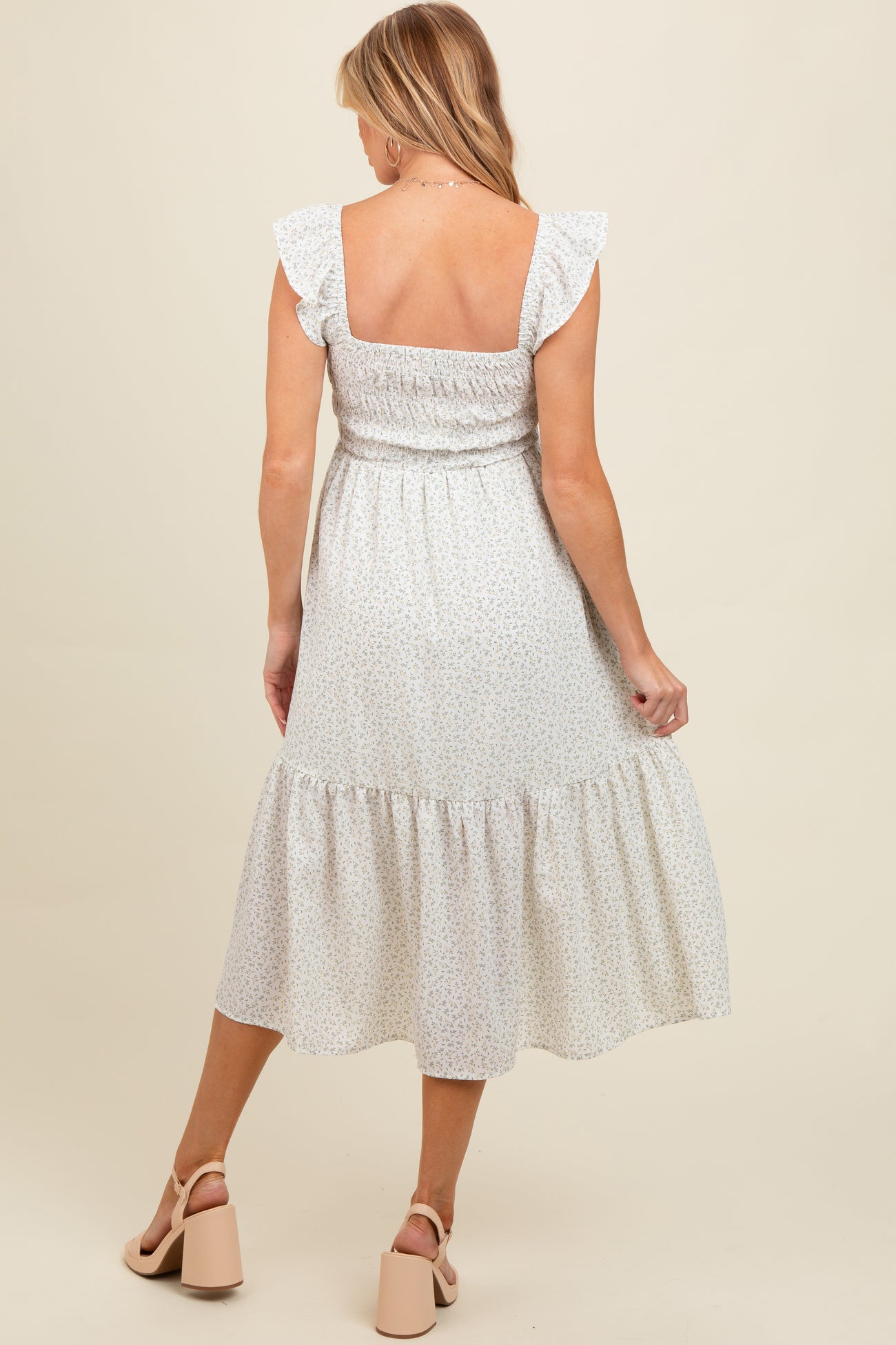 woman wearing a white floral maternity maxi dress with ruffle sleeves and a tiered skirt, showing her back