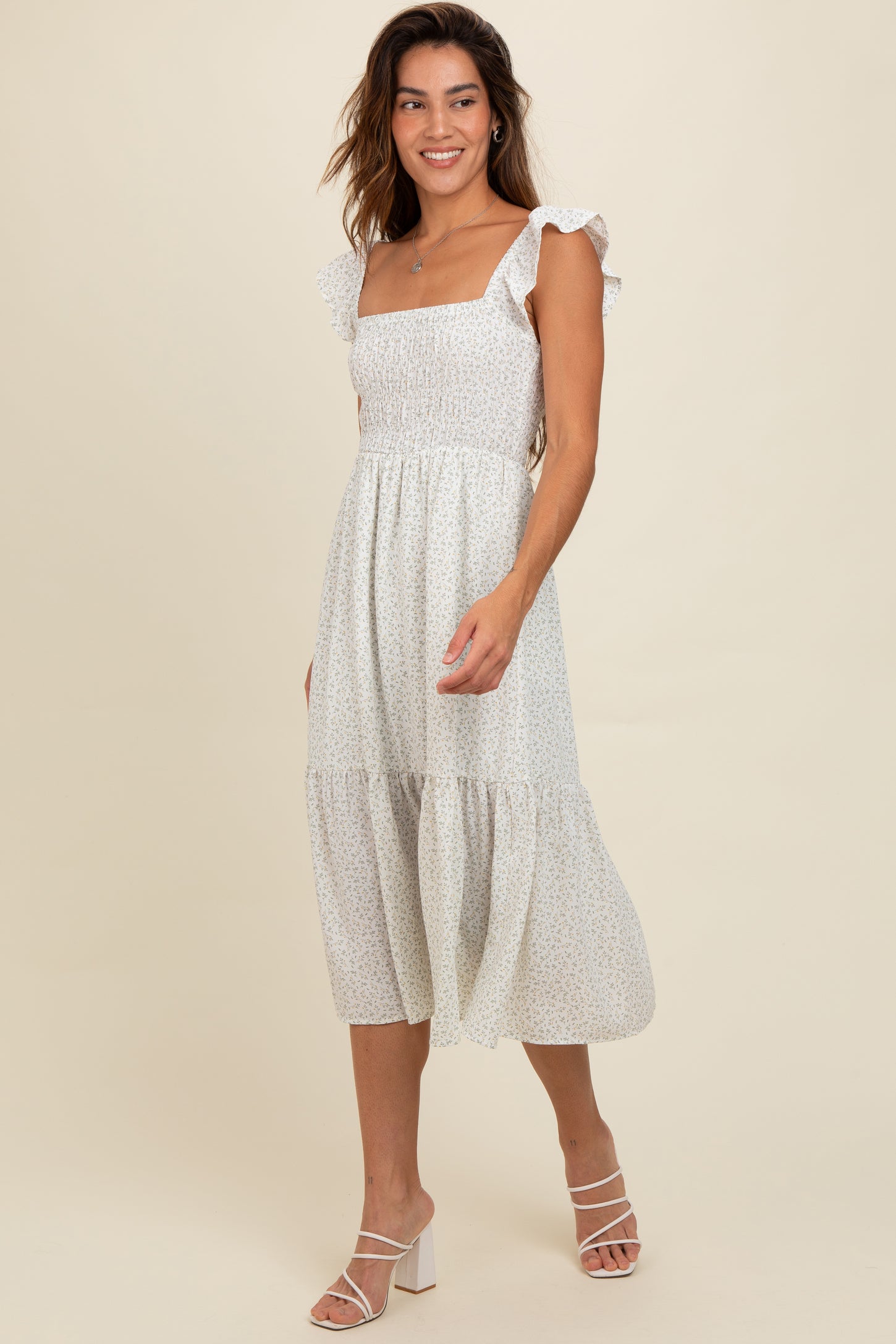 woman wearing a white floral midi dress with ruffle sleeves and a smocked bodice, walking on a plain background