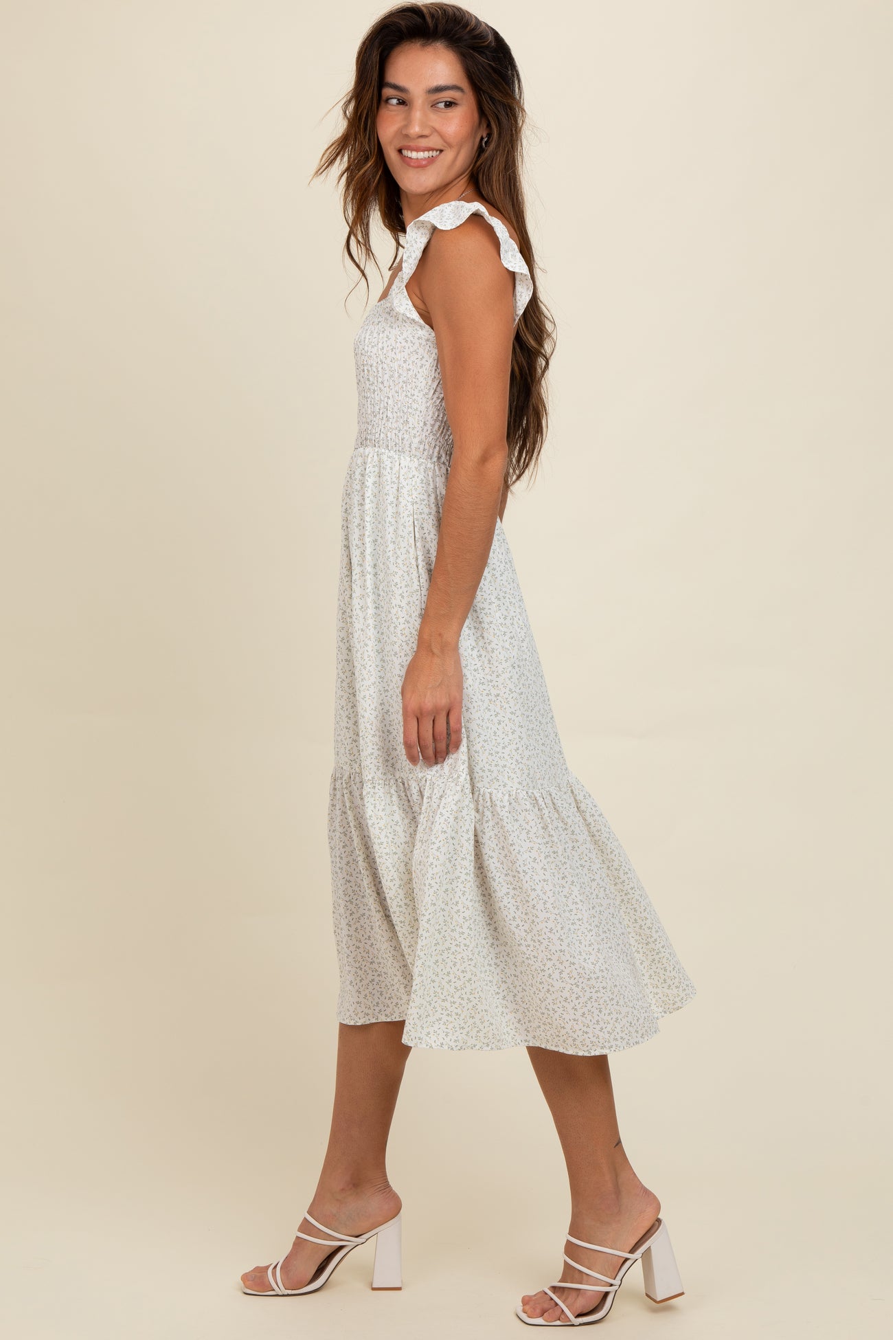 woman wearing a white floral midi dress with ruffle straps and a tiered skirt, standing in profile
