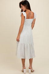 woman wearing a white floral midi dress with ruffled sleeves and a tiered skirt, styled with white block-heel sandals