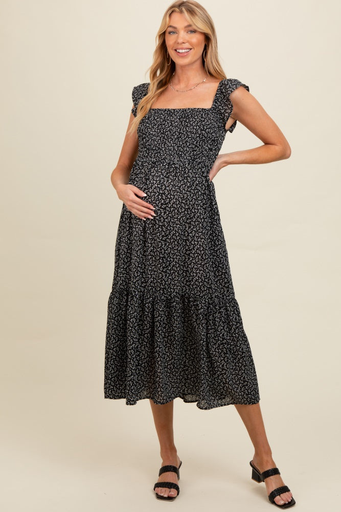 woman wearing a black floral maternity dress with ruffled straps and a tiered skirt, holding her baby bump