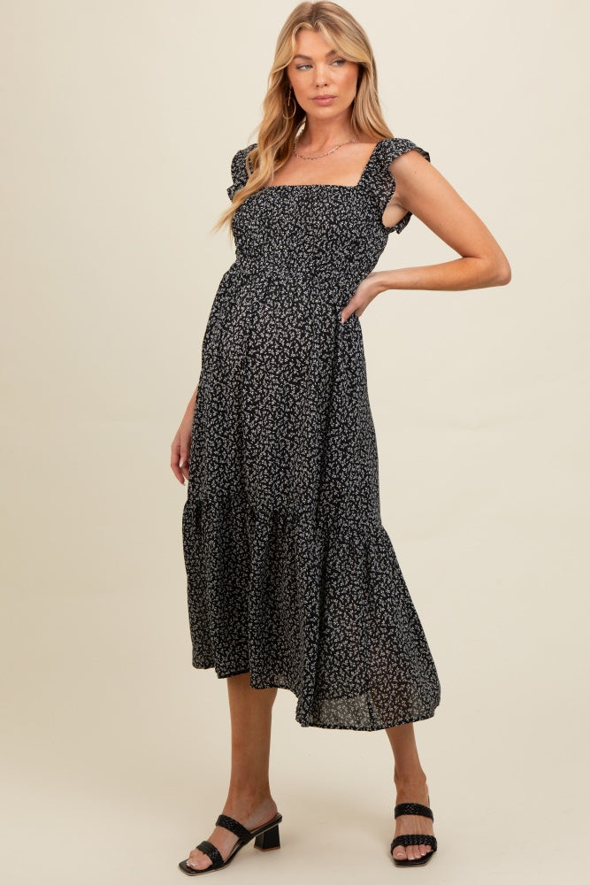 woman wearing a black floral maternity dress with ruffled sleeves and a tiered skirt, highlighting her baby bump