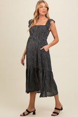 woman wearing a black floral maternity dress with ruffled straps and pockets, showcasing her baby bump