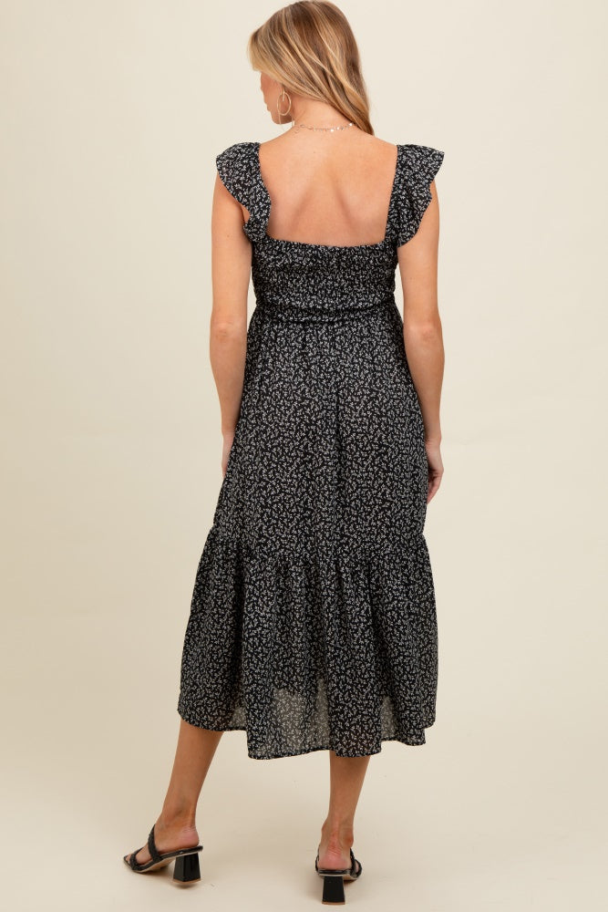 woman wearing a black floral print maternity dress with ruffle sleeves and a tiered skirt, showing a baby bump from the back