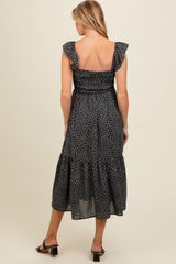 woman wearing a black floral print maternity dress with ruffle sleeves and a tiered skirt, showing a baby bump from the back