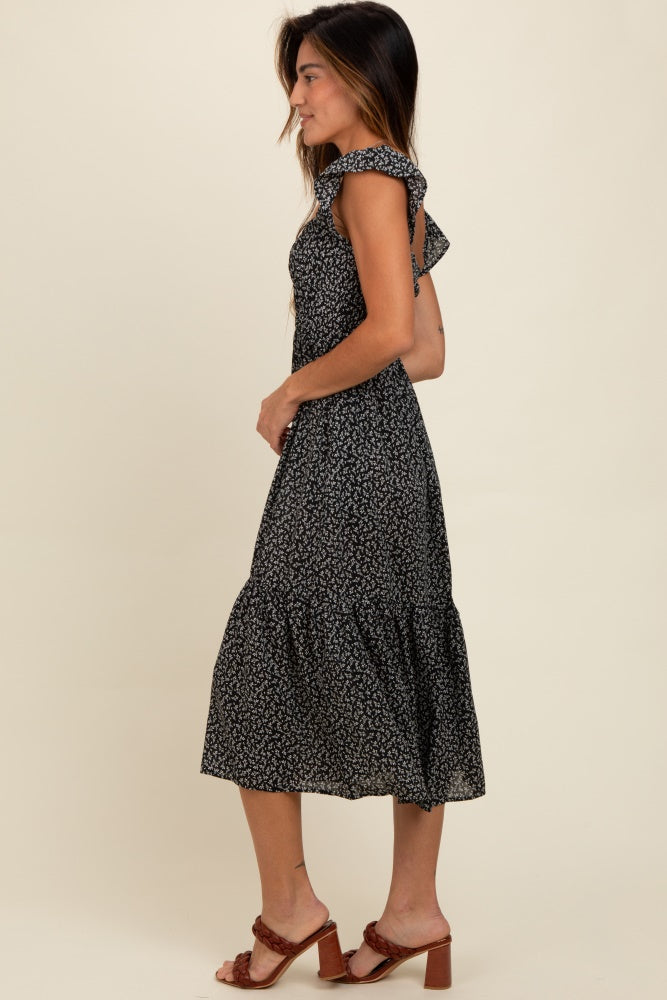 woman wearing a black floral print midi dress with ruffled shoulders and a tiered skirt