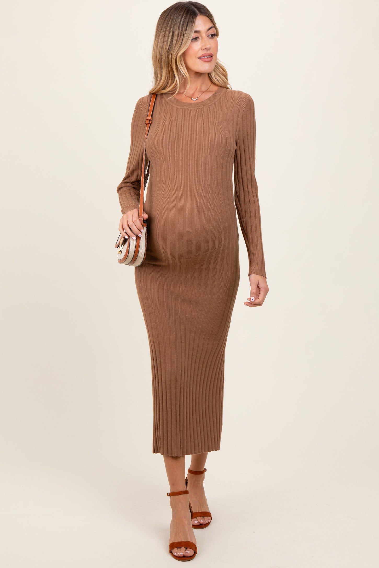woman wearing a brown ribbed maternity dress with long sleeves and a visible baby bump, carrying a crossbody bag