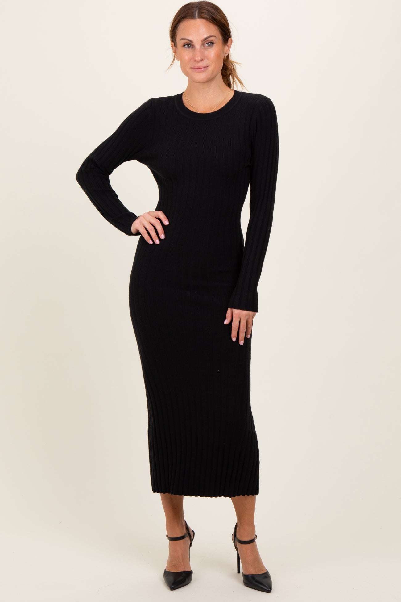 woman wearing a black ribbed long sleeve midi dress with a fitted silhouette and styled with black high heels
