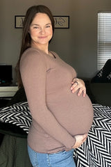 woman wearing a brown long sleeve maternity top and holding her baby bump