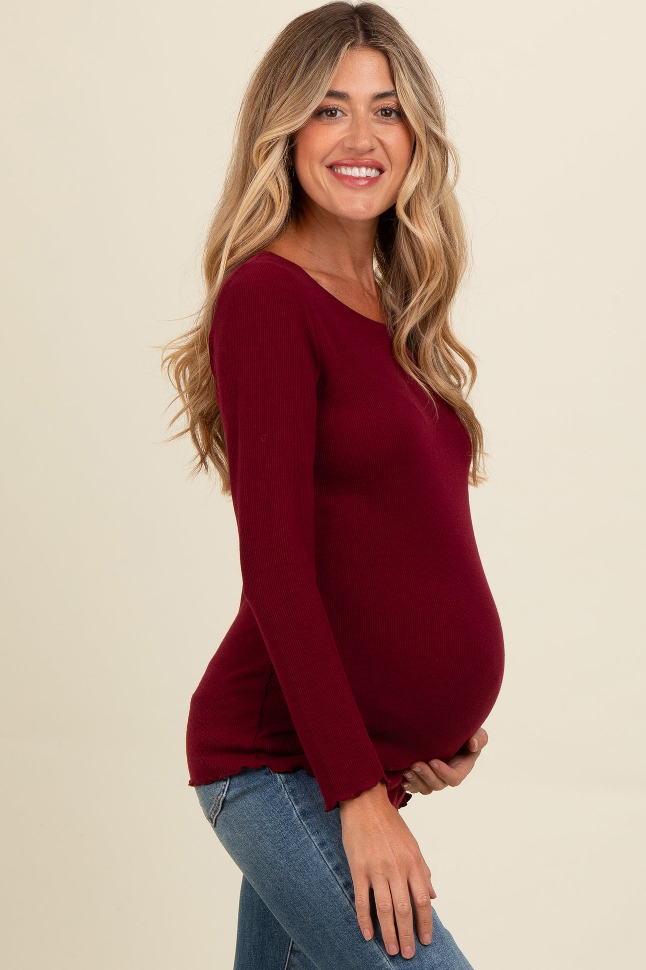 woman wearing a burgundy long sleeve maternity top and holding her baby bump