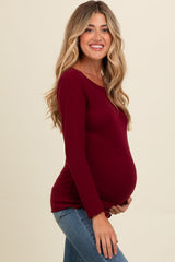 woman wearing a burgundy long sleeve maternity top and holding her baby bump