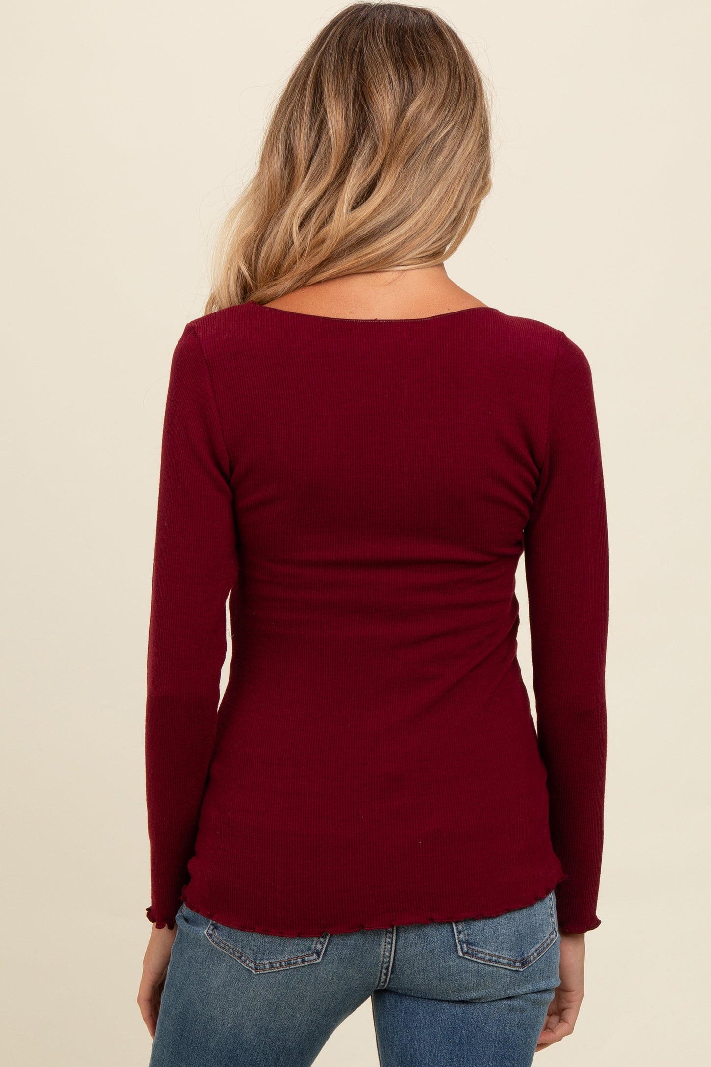 woman wearing a burgundy long sleeve maternity top, fitted style, seen from the back, showing a smooth silhouette