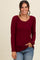 woman wearing a burgundy long sleeve ribbed top with a scoop neckline and side slits, styled with blue jeans