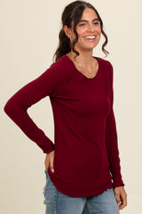woman wearing a burgundy long sleeve ribbed top with a curved hemline and a relaxed fit