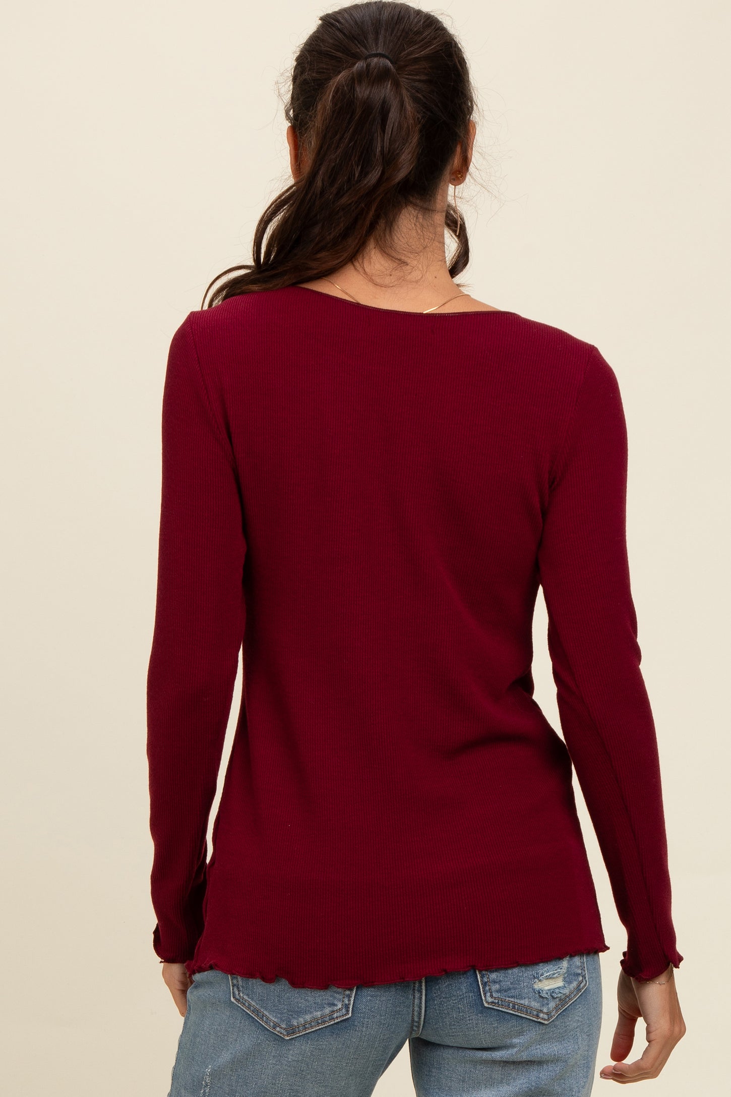 woman wearing a burgundy long sleeve ribbed top with a scoop back and raw hem details