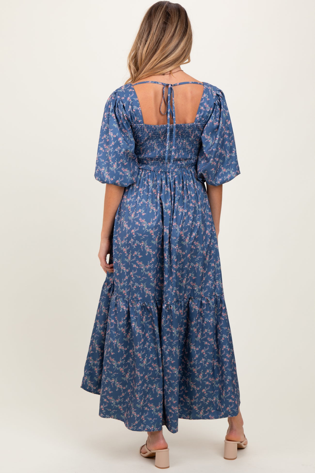 woman wearing a blue floral maternity dress with smocked bodice and puff sleeves, showcasing the back view