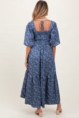 woman wearing a blue floral maternity dress with smocked bodice and puff sleeves, showcasing the back view
