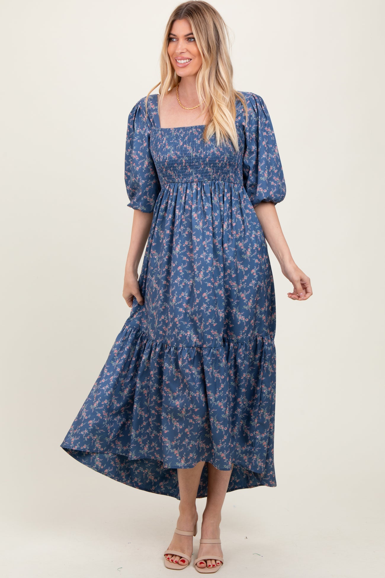 woman wearing a blue floral maxi dress with puff sleeves and a tiered hem, standing confidently