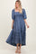 woman wearing a blue floral maxi dress with puff sleeves and a tiered hem, standing confidently