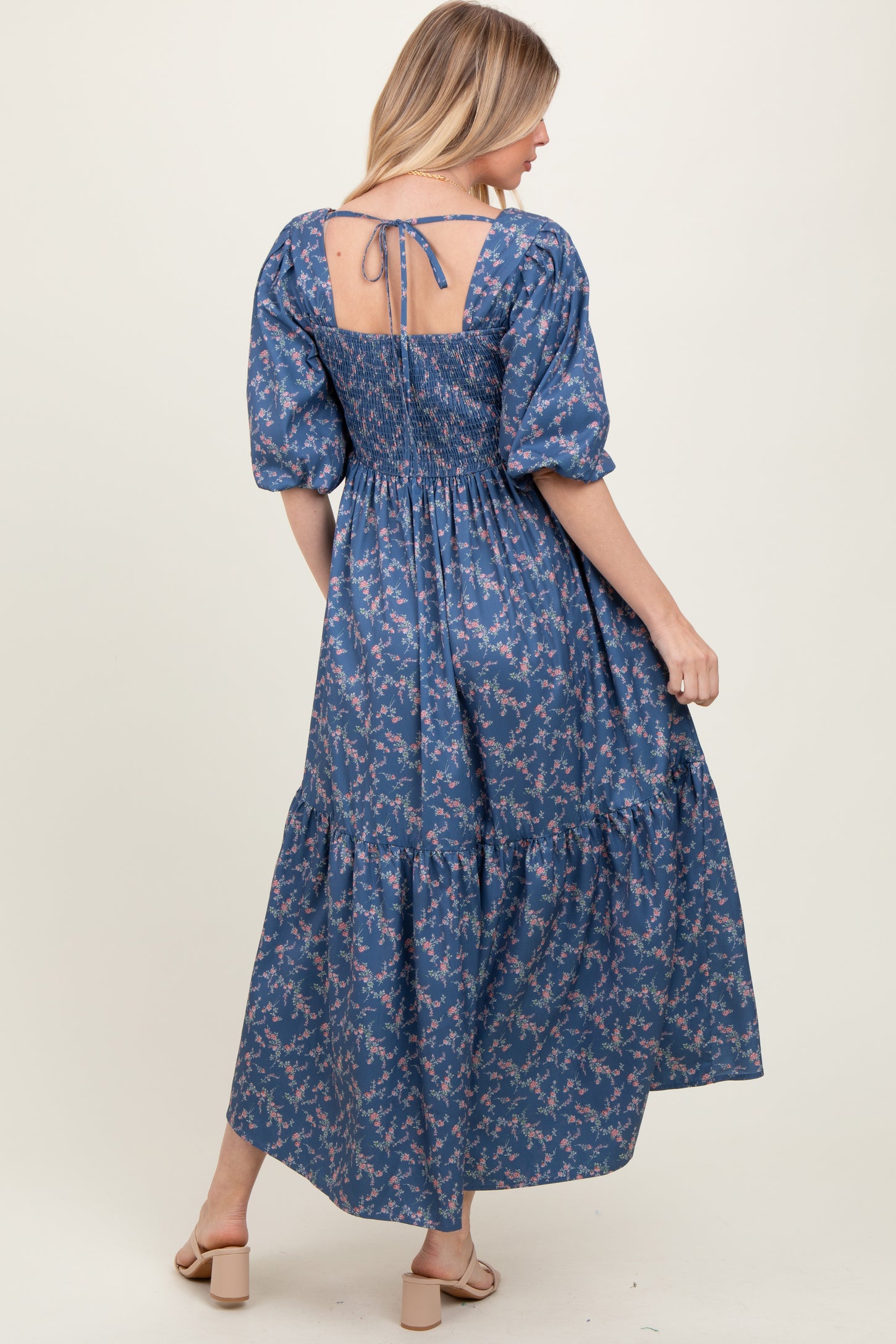 woman wearing a blue floral maxi dress with puff sleeves and a smocked back, turning to show the back detail