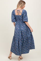 woman wearing a blue floral maxi dress with puff sleeves and a smocked back, turning to show the back detail