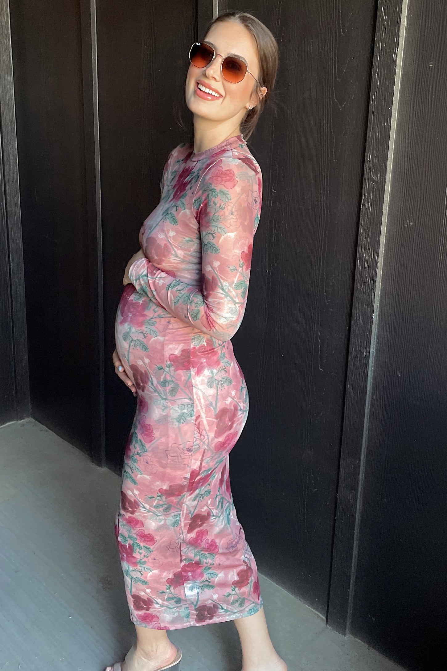 woman wearing a floral long sleeve maternity dress and gently touching her baby bump