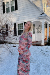 woman wearing a floral long sleeve maternity dress and showing her baby bump outside a house with snow on the ground