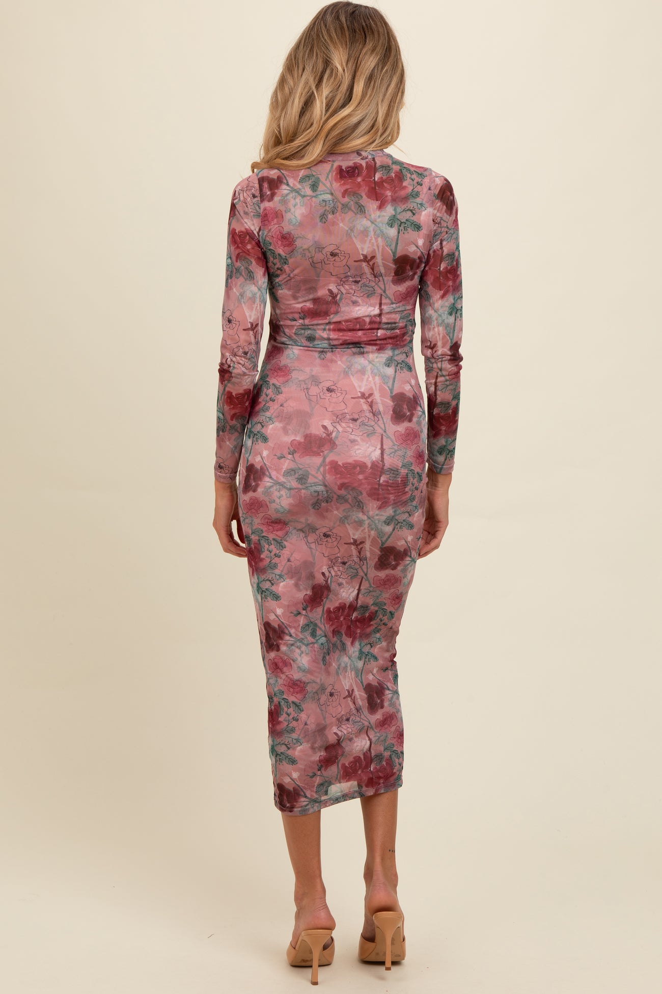 woman wearing a fitted floral long sleeve maternity dress in pink and green with a mid-calf length