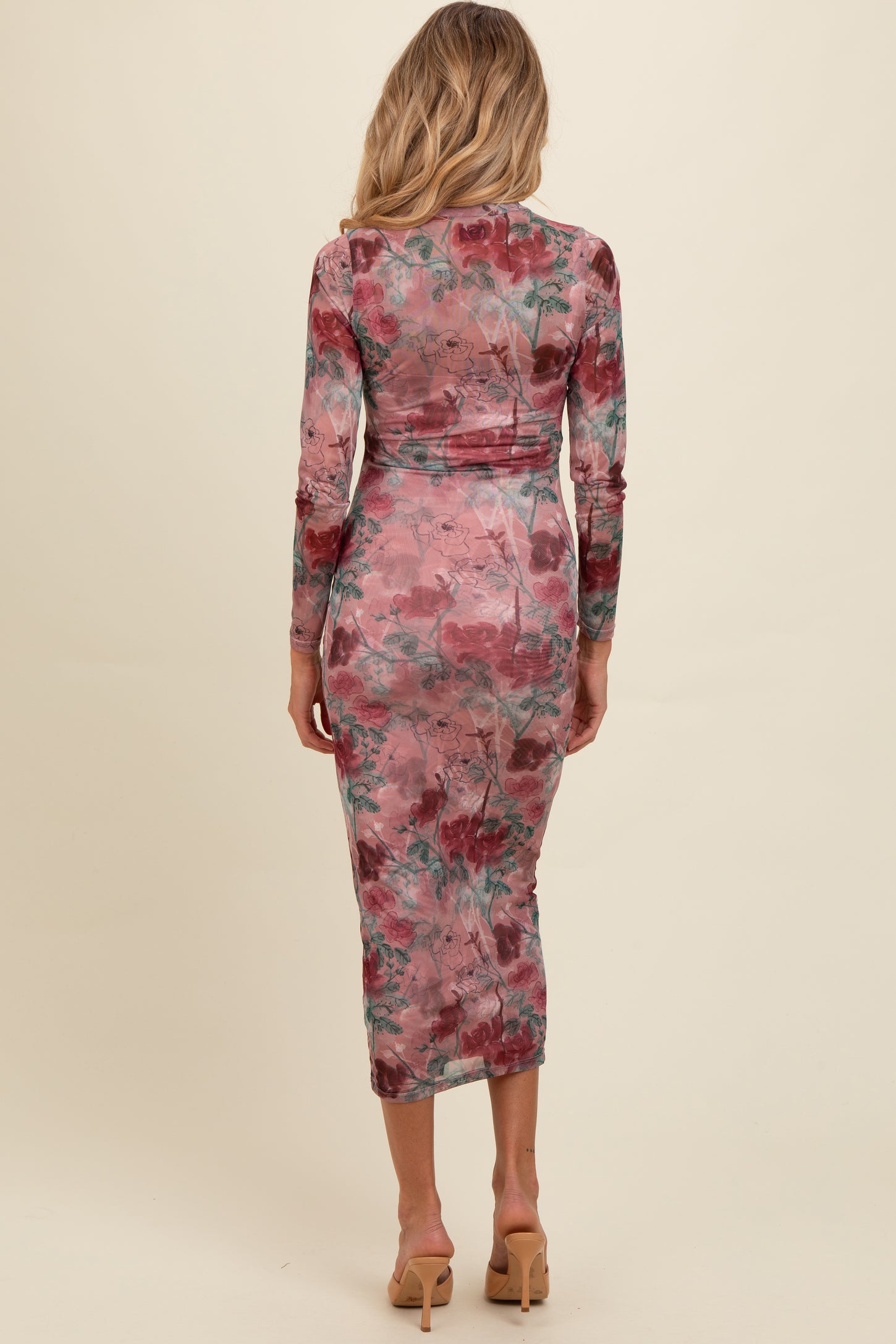 woman wearing a fitted floral long sleeve maternity dress in pink and green with a mid-calf length