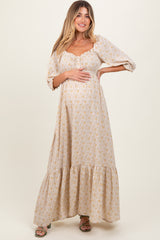 woman wearing a beige floral maternity maxi dress with puff sleeves and a gathered bust, holding her baby bump