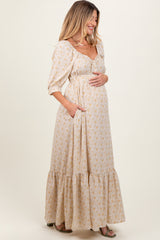 woman wearing a cream floral maternity maxi dress with puff sleeves and pockets, holding her baby bump