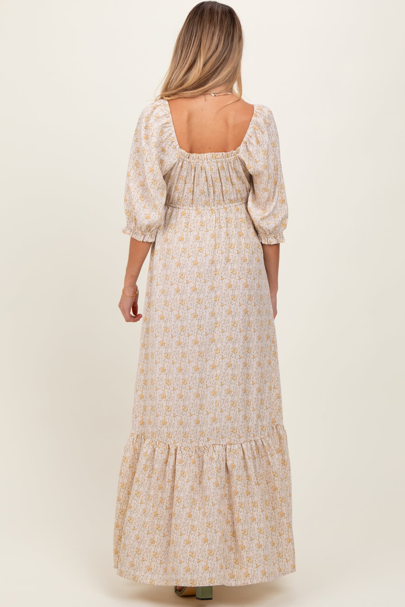 woman wearing a beige floral maternity maxi dress with puff sleeves and a ruffled hem, shown from the back